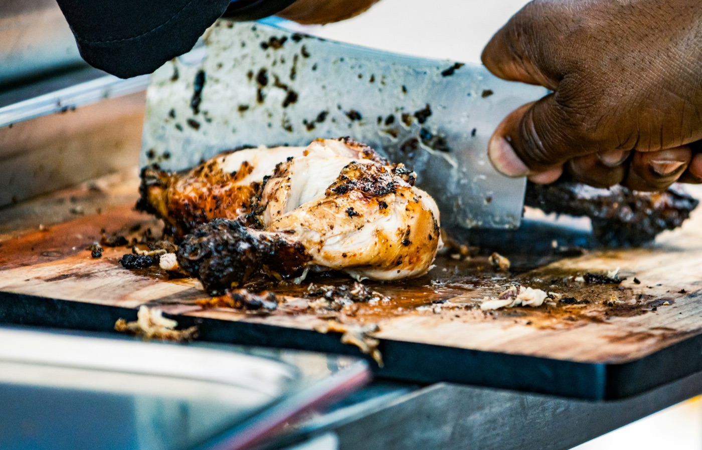 Hands cleaving charred jerk chicken on the board